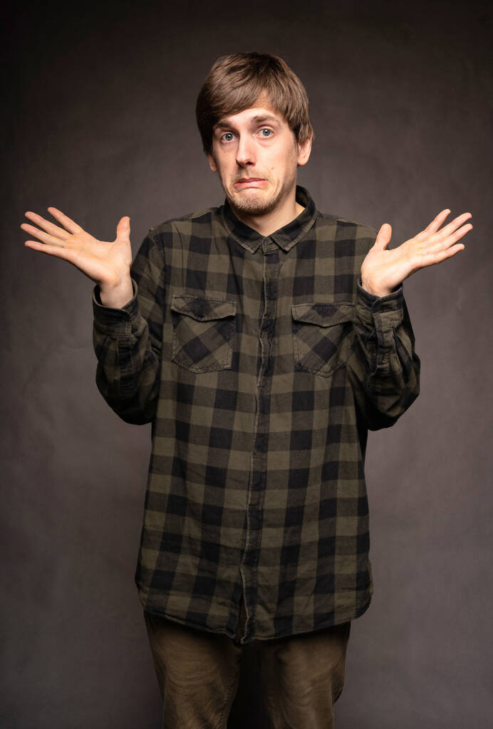 Young handsome tall slim white man with brown hair not knowing what to do with flannel shirt on grey background - Zdjęcie, obraz