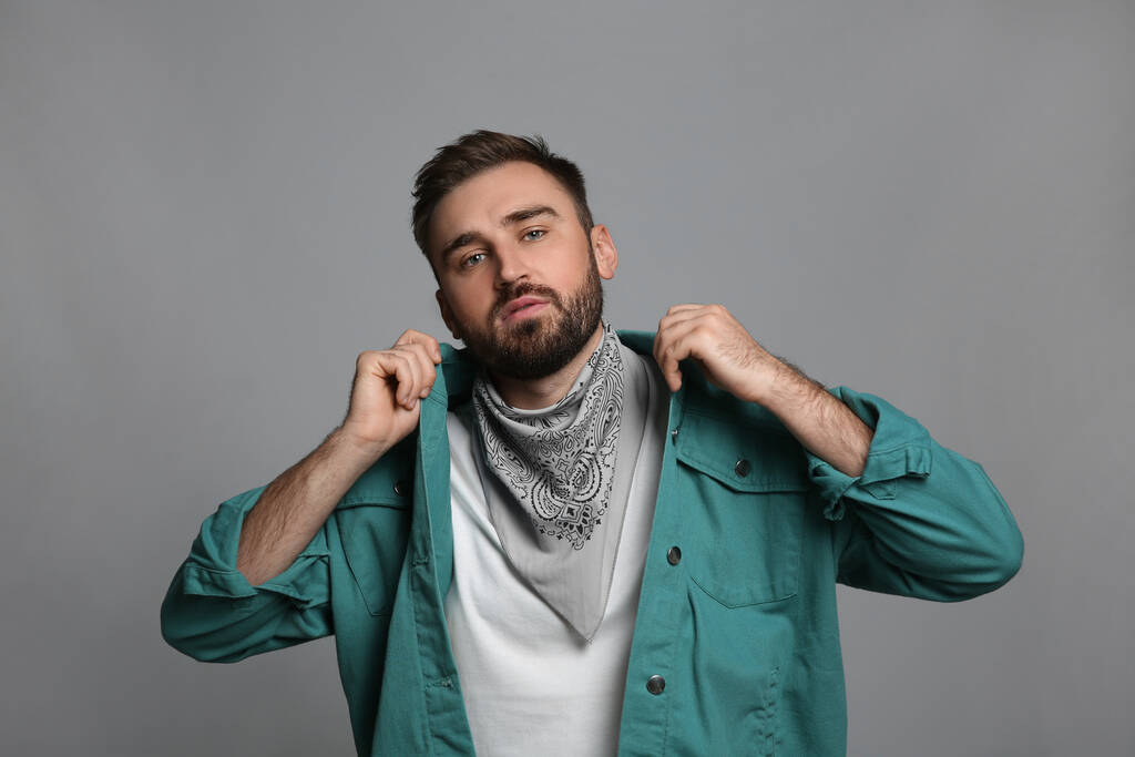 Módní mladý muž ve stylovém oblečení s šátkem na šedém pozadí - Fotografie, Obrázek