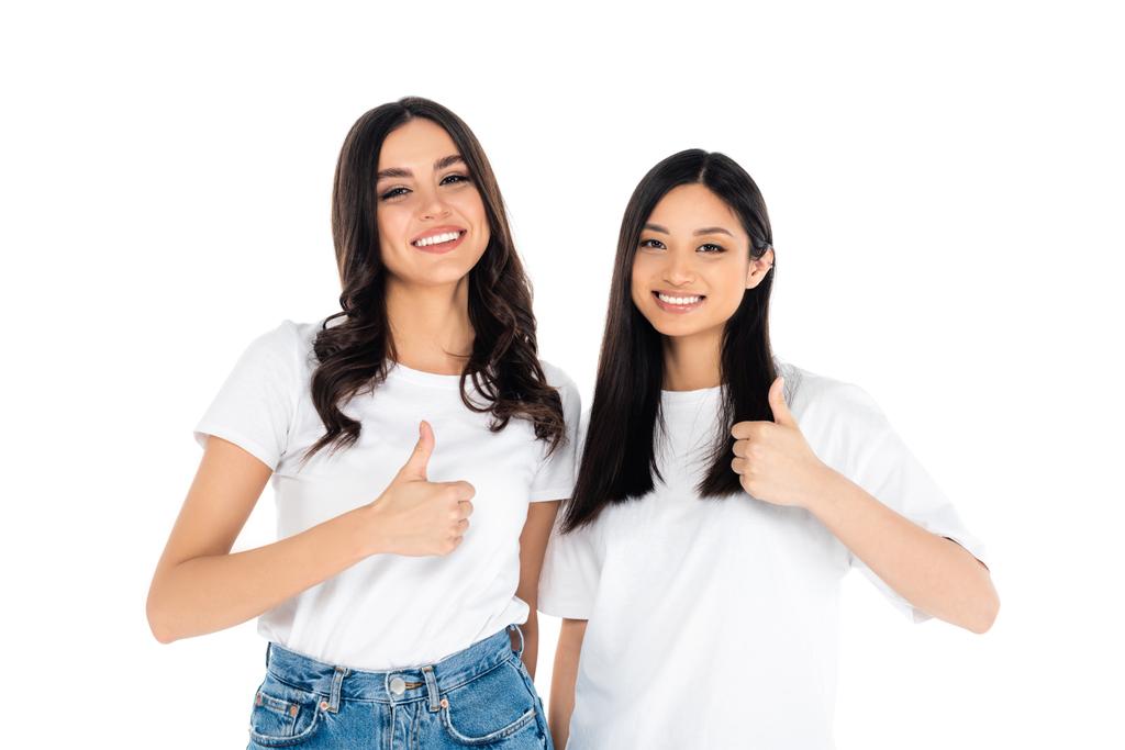 young brunette multiethnic women showing thumbs up while smiling at camera isolated on white - Фото, изображение