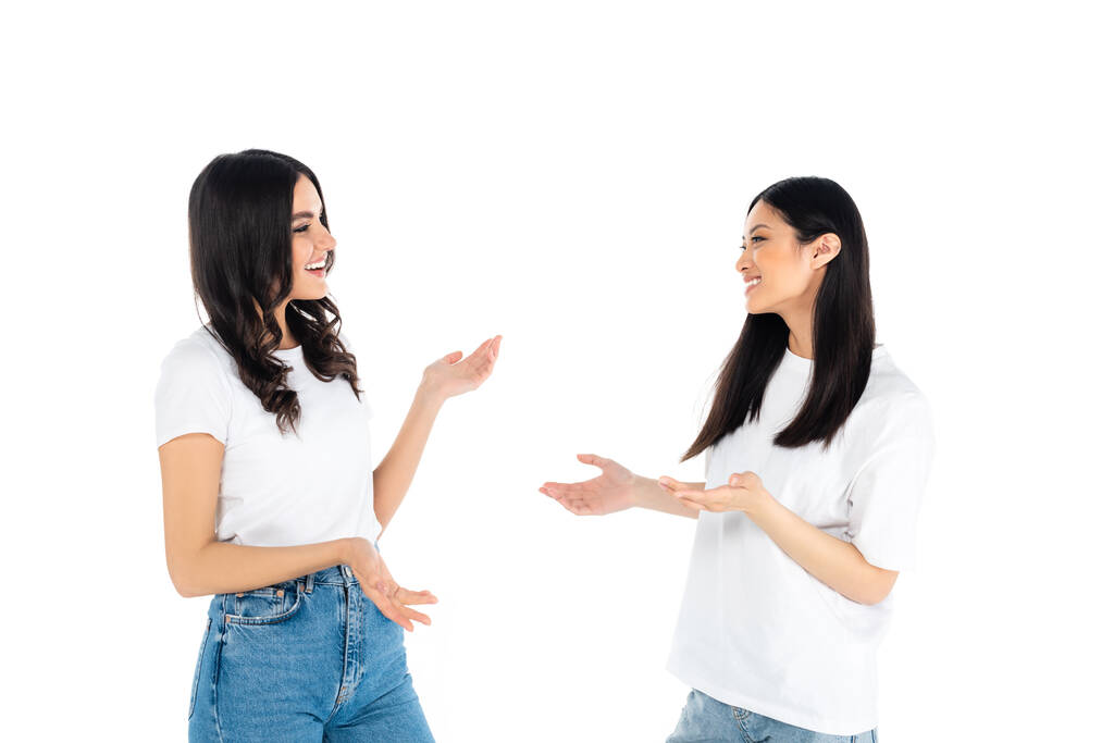 cheerful interracial women in t-shirts and jeans talking isolated on white - Фото, изображение