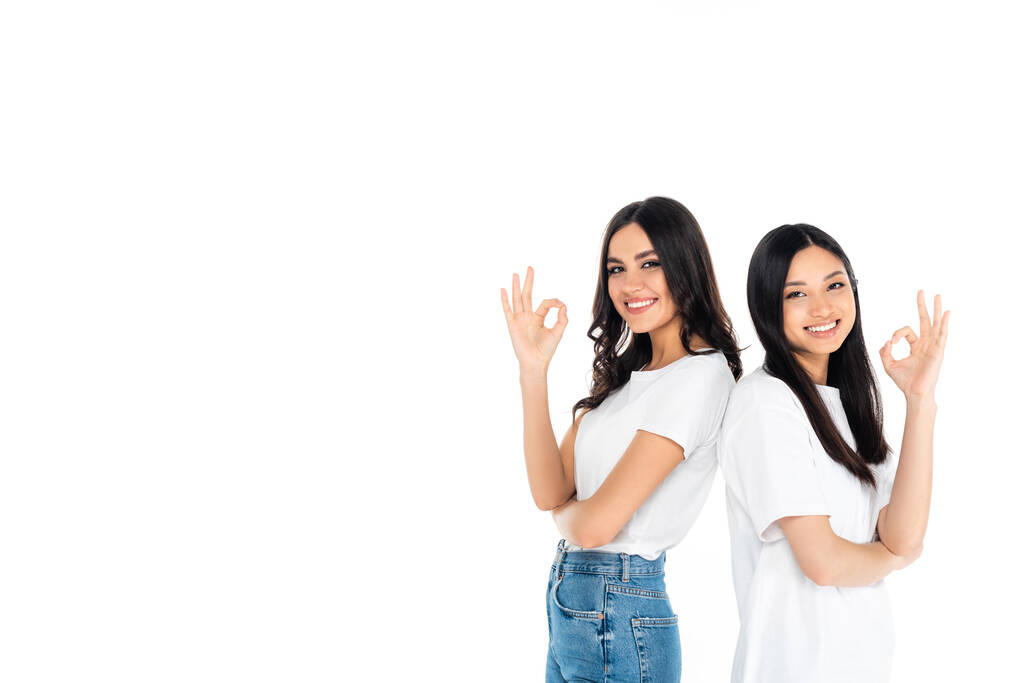 brunetka multietnické ženy ukazující v pořádku značky a usmívající se na kameru izolované na bílém - Fotografie, Obrázek