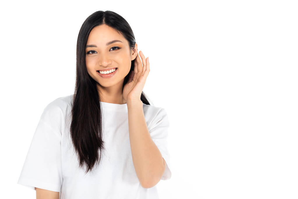 veselá asijské žena při pohledu na kameru a upevnění vlasy izolované na bílém - Fotografie, Obrázek