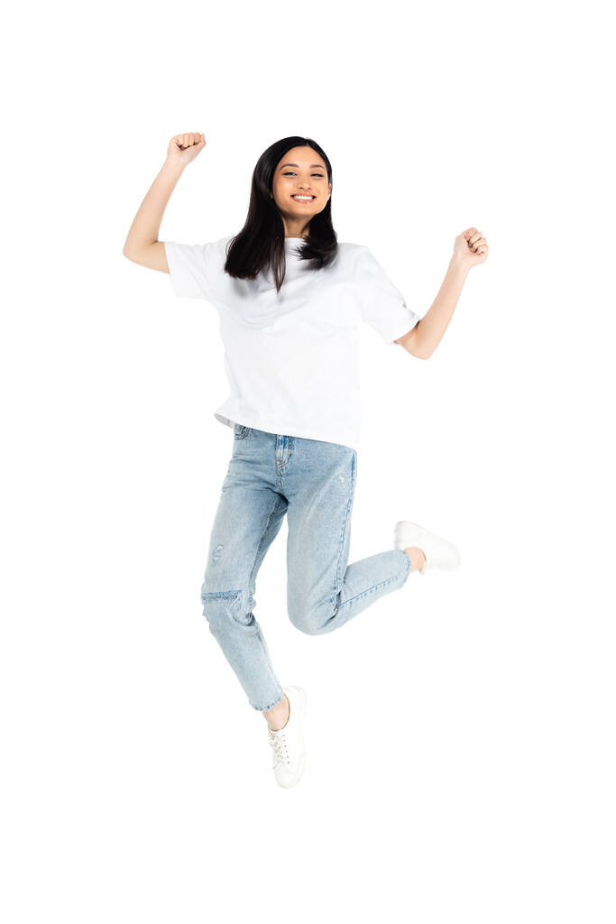 pełny długość widok wesoły azjatycki kobieta w t-shirt i dżinsy lewitujące izolowane na biały - Zdjęcie, obraz