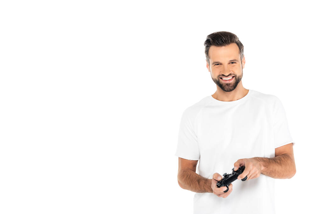 KYIV, UKRAINE - DECEMBER 5, 2021: joyful man in t-shirt gaming with joystick isolated on white - 写真・画像
