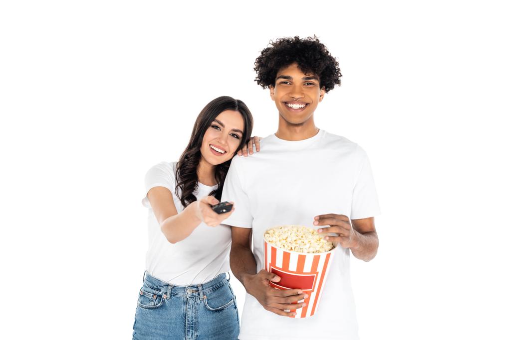 smiling woman clicking tv channels near happy african american man with popcorn isolated on white - Photo, Image