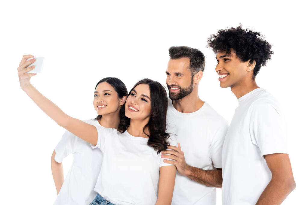 pleased woman taking selfie with interracial friends on mobile phone isolated on white - Photo, Image