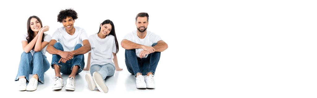 happy multicultural men and women in jeans sitting and looking at camera on white, banner - Foto, immagini