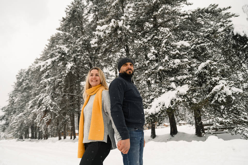 Attractive man and woman cuddling in the frosty forest. Adult couple in sweaters have fun on walk. Romantic date in winter time.Winter lovestory - Фото, изображение