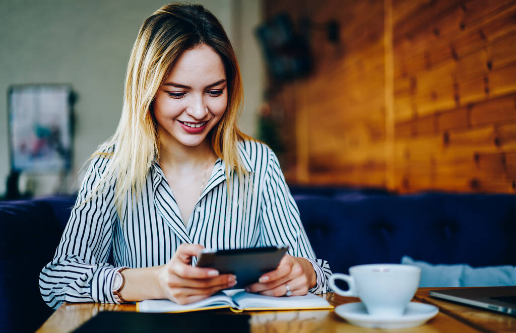 Χαρούμενη hipster κορίτσι με ψηφιακό ebook χαμογελώντας κατά την ανάγνωση κειμένου κατά τη διάρκεια του ελεύθερου χρόνου στην καφετέρια, ευτυχισμένη γυναίκα Caucaisan με σύγχρονη τεχνολογία αφής δικτύωσης social media στην καφετέρια - Φωτογραφία, εικόνα