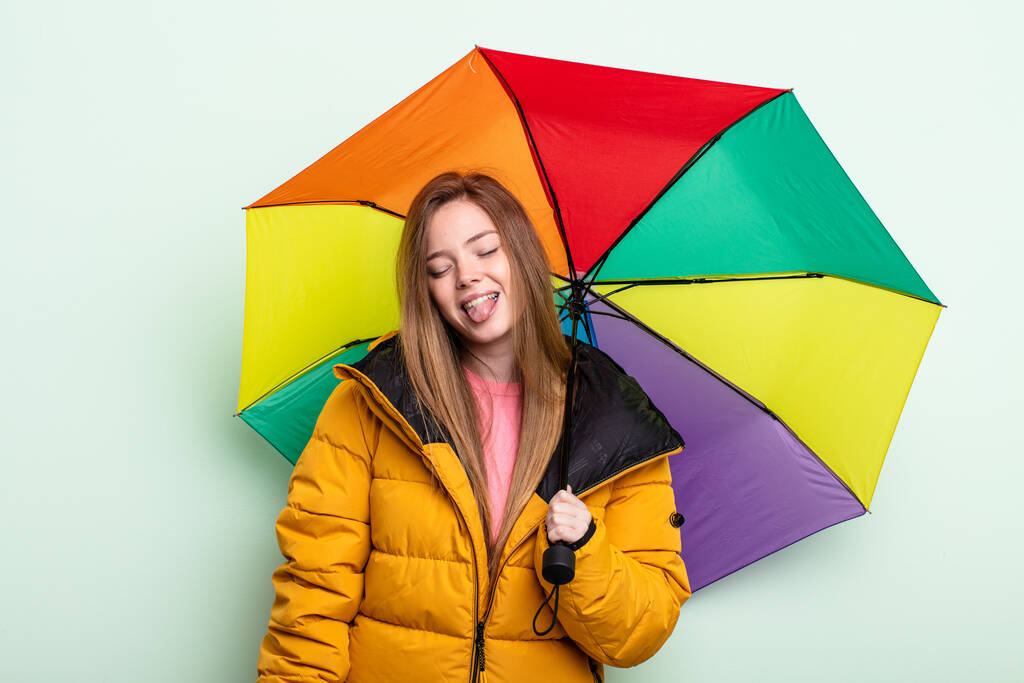 pelirroja mujer con actitud alegre y rebelde, bromeando y sacando la lengua. concepto de paraguas - Foto, imagen