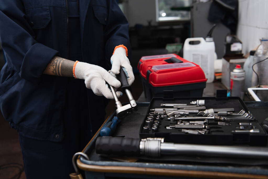Обрізаний вид ручної роботи, що тримає інструмент біля гайкових ключів у автосервісі
 - Фото, зображення