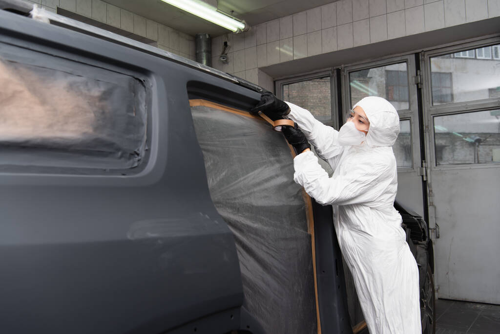 Lavoratrice in tuta hazmat che applica nastro adesivo sull'auto in servizio  - Foto, immagini