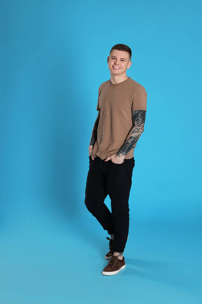 Hymyilevä nuori mies, jolla on tatuoinnit vaaleansinisellä taustalla - Valokuva, kuva