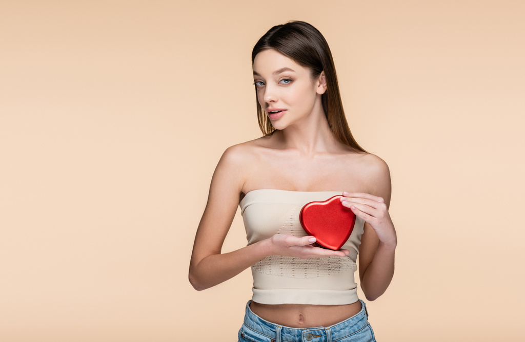brunette nainen tilalla punainen sydämen muotoinen laatikko eristetty beige  - Valokuva, kuva