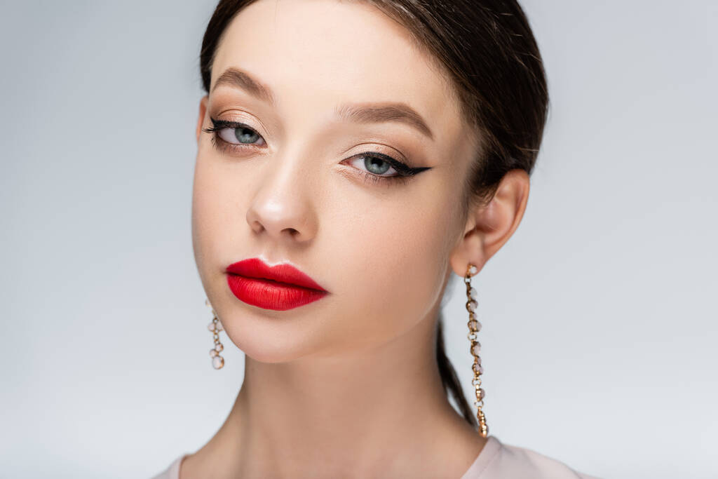 pretty young woman in earrings with red lips looking at camera isolated on grey - 写真・画像