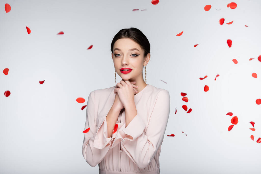 young and sensual woman with bright makeup near falling rose petals on grey - Photo, Image