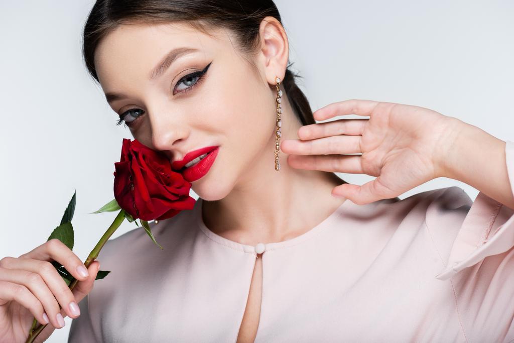 brunette woman in earrings holding red rose isolated on grey - Photo, Image