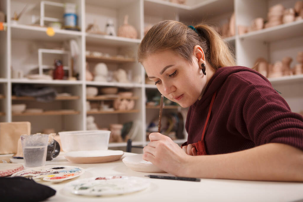 陶芸教室で働く女性作家、陶芸皿を描く、コピースペース - 写真・画像