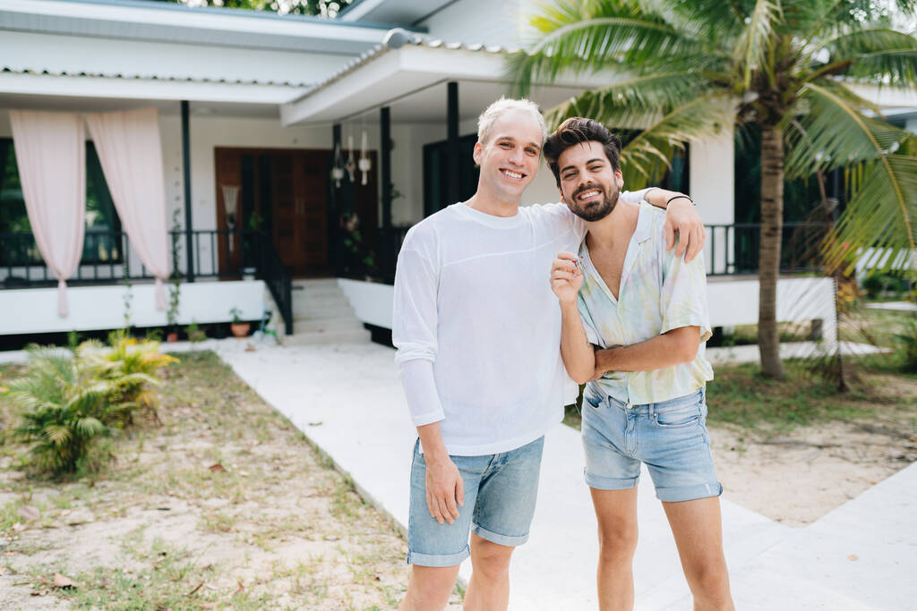Gay couple standing in front of their house and holding keys of thier new house - Foto, imagen