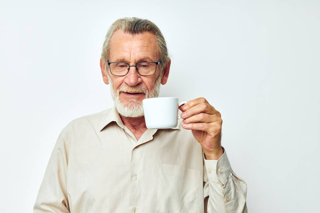 ένας ηλικιωμένος άντρας να κρατάει μια κούπα σε λευκό φόντο και να χαμογελάει - Φωτογραφία, εικόνα