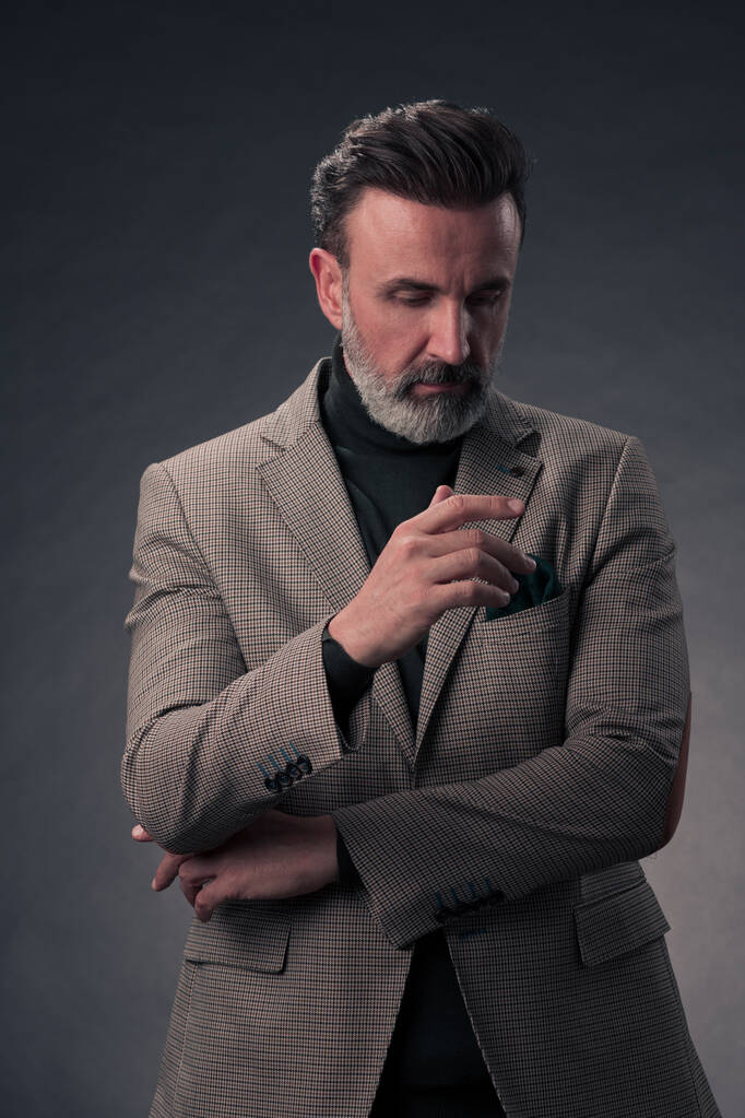 Portrét stylového elegantního staršího podnikatele s vousy a neformálním obchodním oblečením ve fotoateliéru izolovaném na tmavém pozadí, který gestikuluje rukama. Kvalitní fotografie - Fotografie, Obrázek