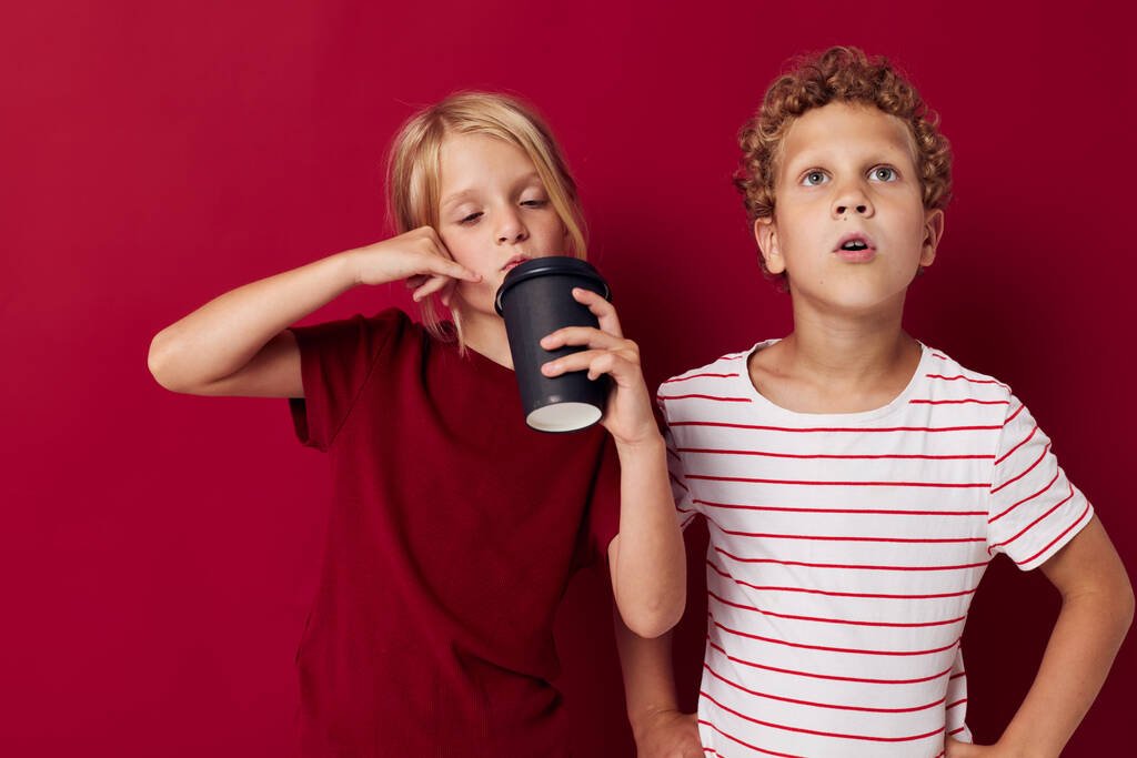 boy and girl are standing next to a disposable glass with a drink red background - Photo, Image
