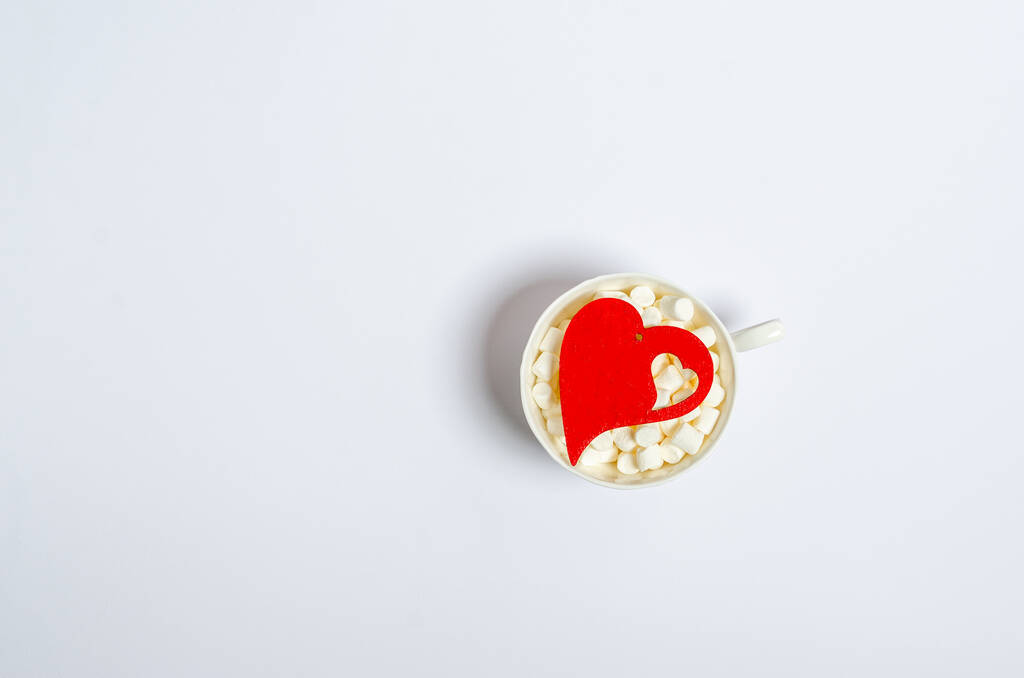 Coração vermelho de madeira em uma xícara com marshmallows em um fundo branco com lugar para texto. - Foto, Imagem