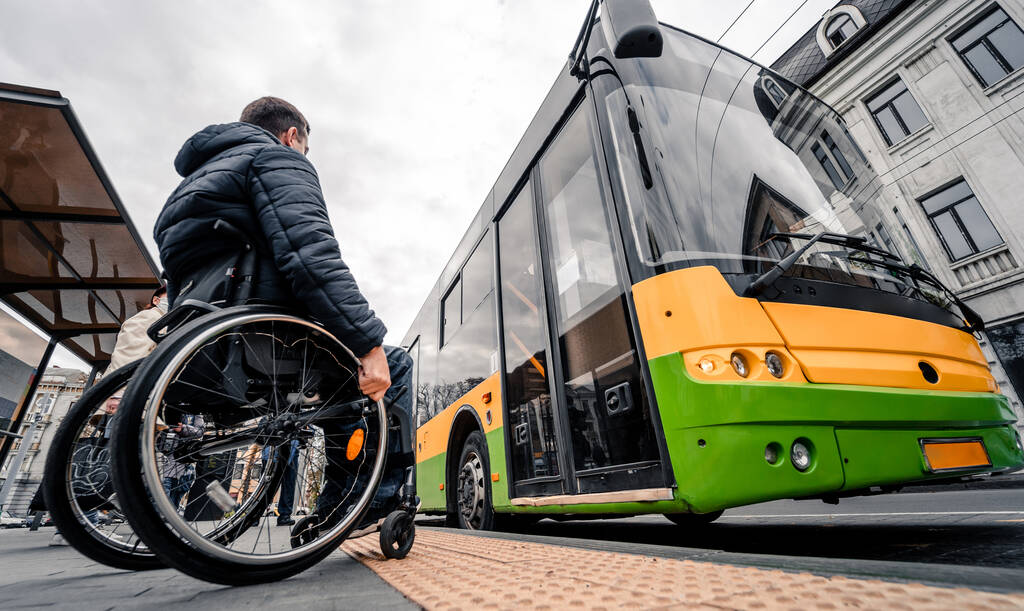 Persona con disabilità fisica in attesa di trasporto urbano con rampa accessibile. - Foto, immagini