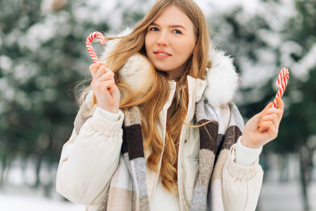 happy woman in winter clothes, having fun while holding Christmas red candies, in a frozen morning outdoors full of snow. Expressing positivity, real fun emotions, looking forward to Christmas - Photo, image