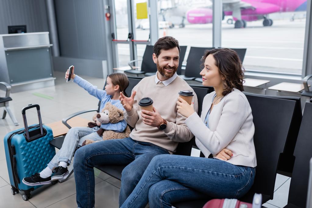 kid taking selfie near happy parents with paper cups and luggage in airport lounge  - Photo, Image