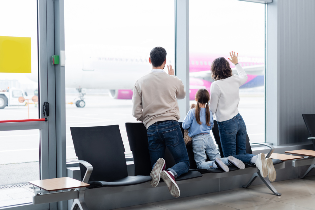πίσω όψη της οικογένειας κουνώντας τα χέρια, ενώ κοιτάζοντας το αεροπλάνο μέσα από το παράθυρο στο αεροδρόμιο - Φωτογραφία, εικόνα