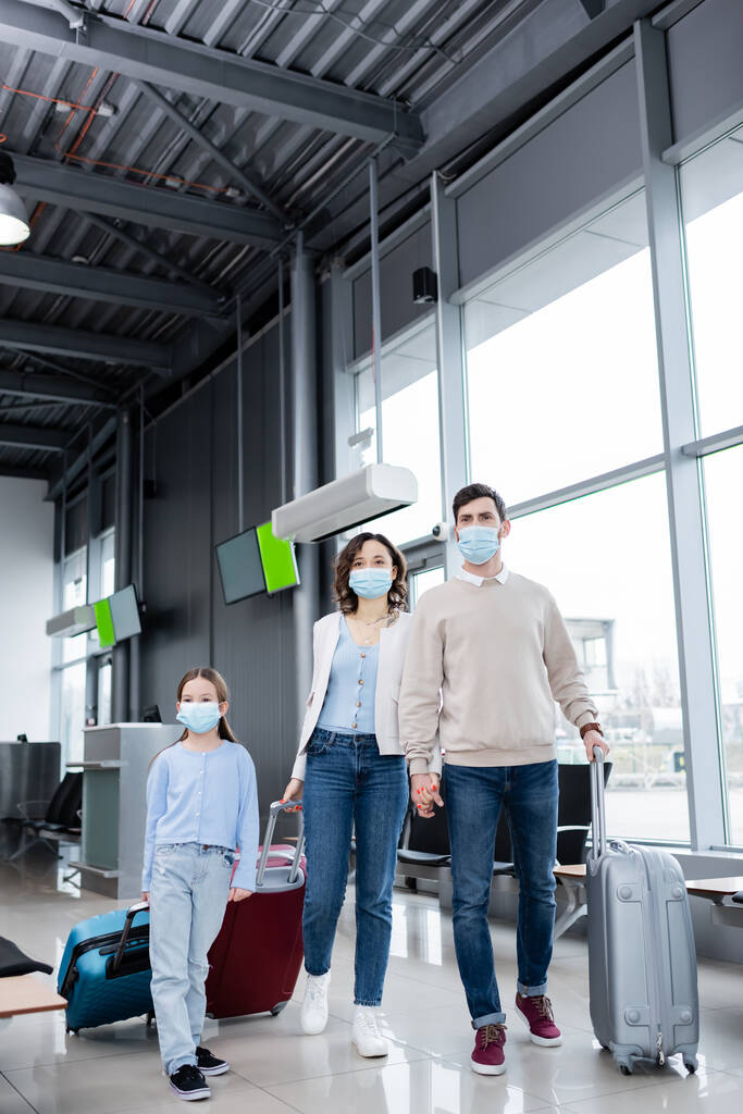 rodzina w maskach medycznych spaceru z walizkami w salonie lotniska  - Zdjęcie, obraz