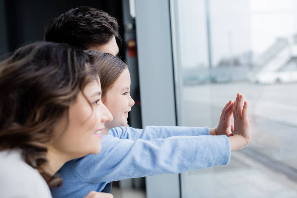 widok z boku wesołej rodziny patrząc na okno na lotnisku  - Zdjęcie, obraz