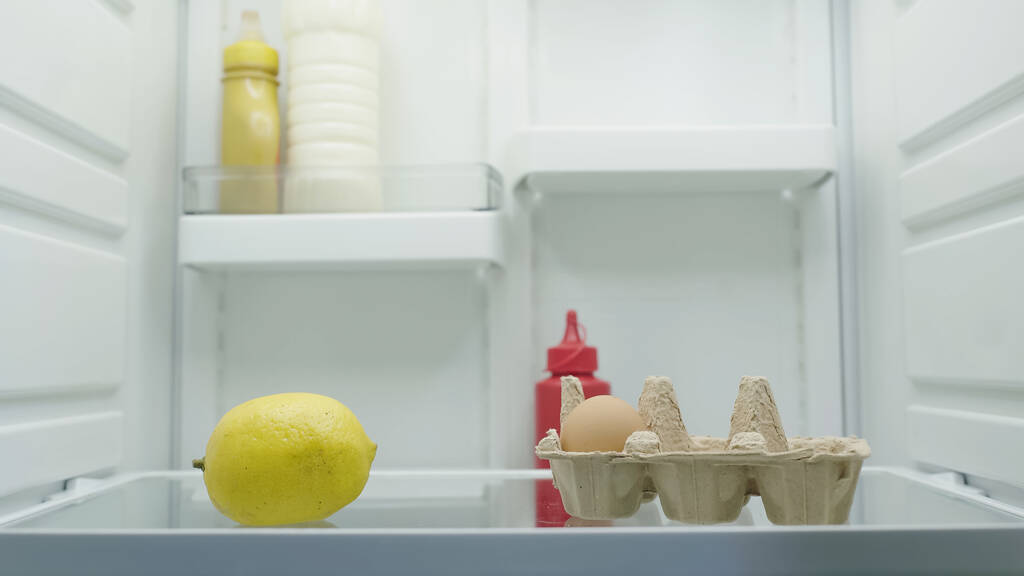 limón entero, huevo, botellas con mayonesa, mostaza y salsa de tomate en nevera - Foto, Imagen