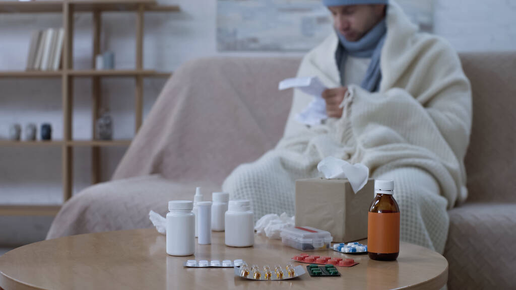 selective focus of medicaments on table near sick man reading medication instruction on blurred background - Foto, Bild