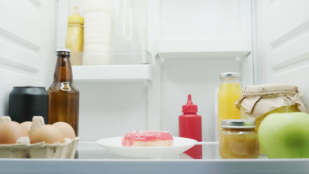 tasty donut, eggs, jars with honey and fruit puree, bottles with drinks, and fresh apple in fridge - Foto, Imagen