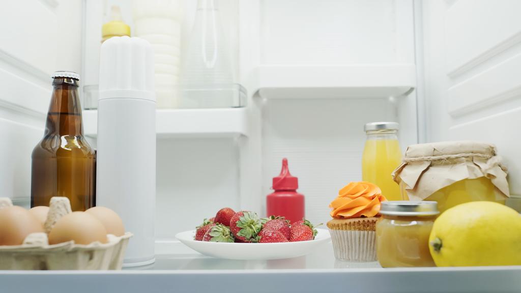 beer, eggs, fresh strawberries, lemon, cupcake, orange juice, honey and sauces in fridge - Fotó, kép