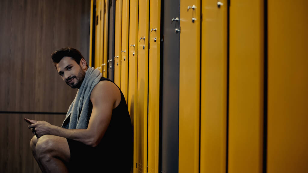happy sportsman holding smartphone in locker room  - Fotoğraf, Görsel