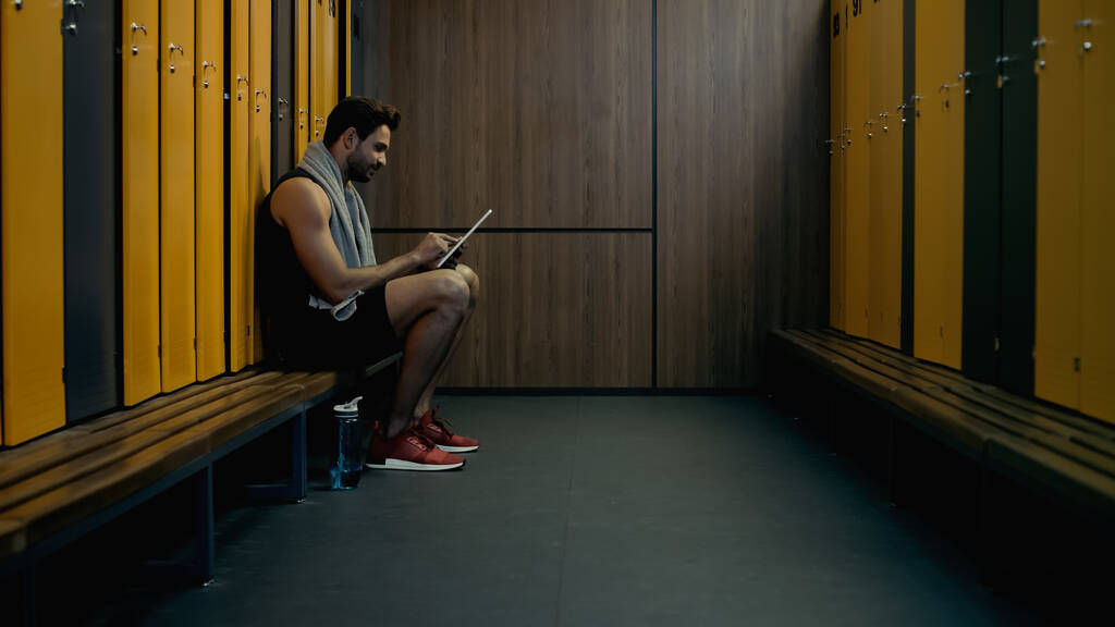 sportsman sitting on bench and using digital tablet in locker room - Φωτογραφία, εικόνα