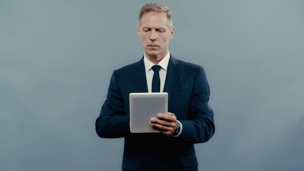 Mature manager in formal wear using digital tablet isolated on grey  - Foto, imagen