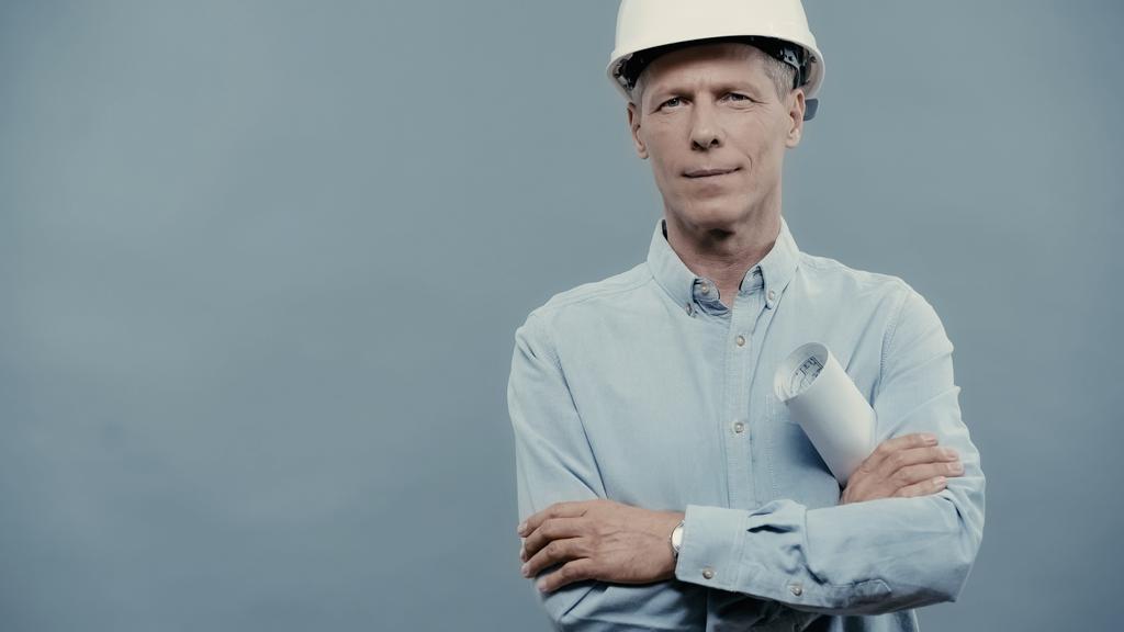 Engineer in hardhat holding blueprint and looking at camera isolated on grey  - Valokuva, kuva