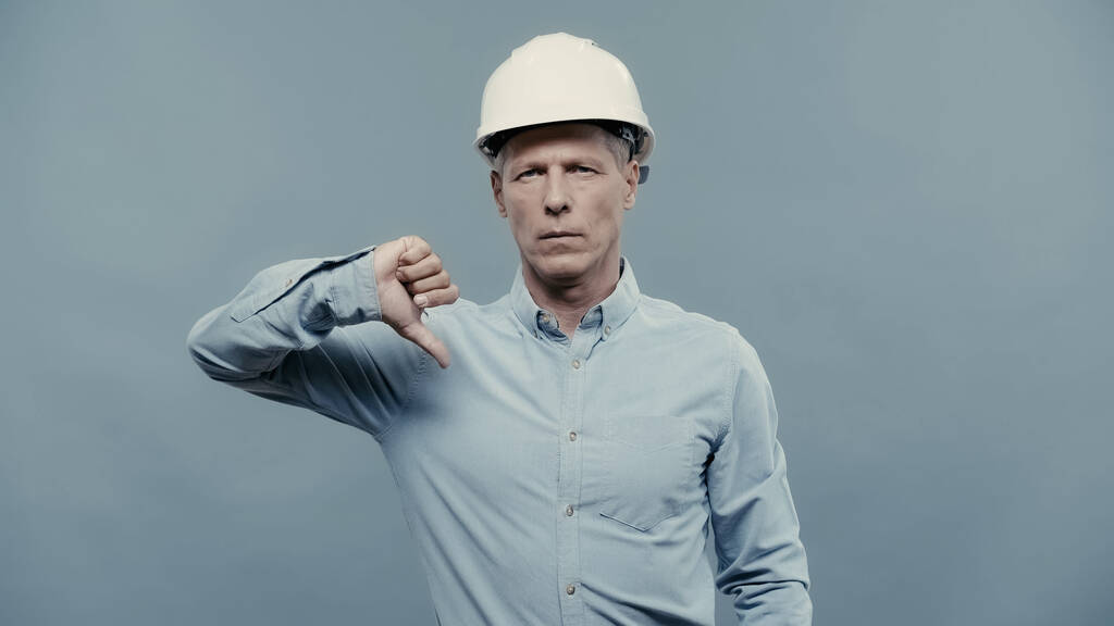 Middle aged engineer in hardhat showing dislike sign isolated on grey  - Fotó, kép