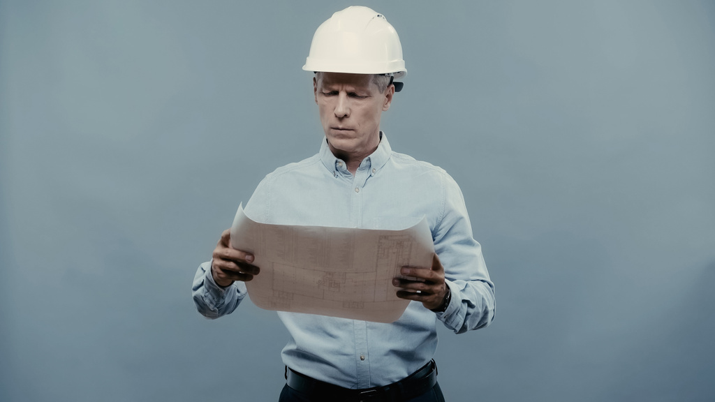 Mature engineer looking at blueprint isolated on grey  - Фото, изображение
