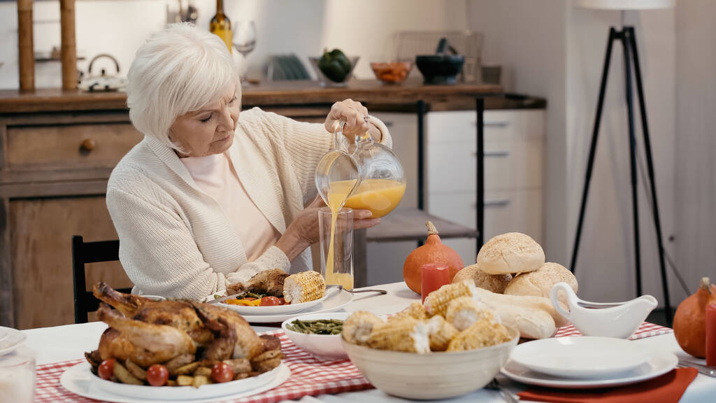 senior man pouring orange juice near roasted turkey, grilled corn and buns on table - Foto, immagini