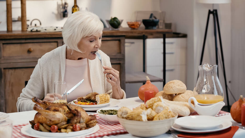 elderly woman having thanksgiving dinner near roasted turkey, grilled corn, orange juice and buns - Fotó, kép