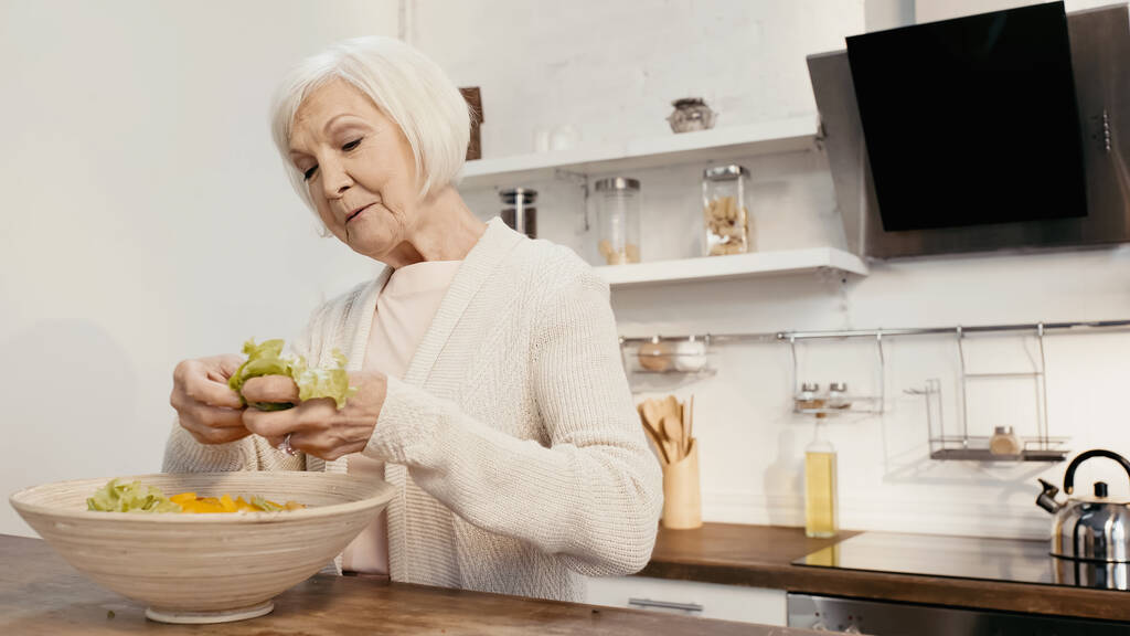 elderly woman adding fresh lettuce to sliced bell pepper while preparing salad for thanksgiving dinner - Photo, Image