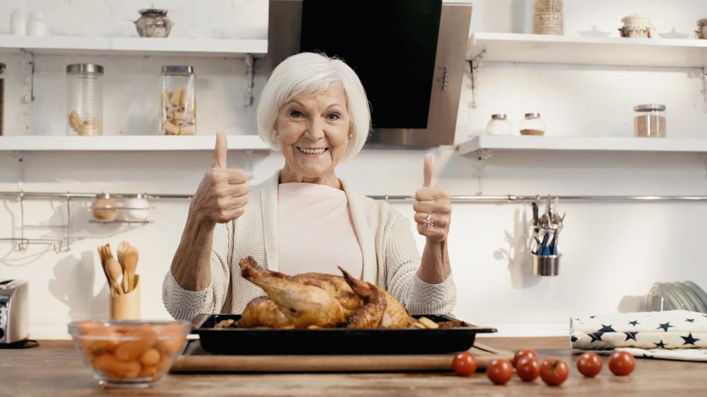 happy woman showing thumbs up near roasted turkey and fresh vegetables on kitchen table - Photo, Image