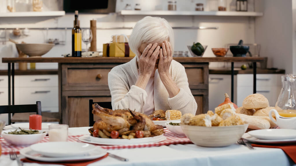καταθλιπτική γυναίκα σκιάζει το πρόσωπο με τα χέρια, ενώ κάθεται στο τραπέζι σερβίρεται με δείπνο Ευχαριστιών - Φωτογραφία, εικόνα