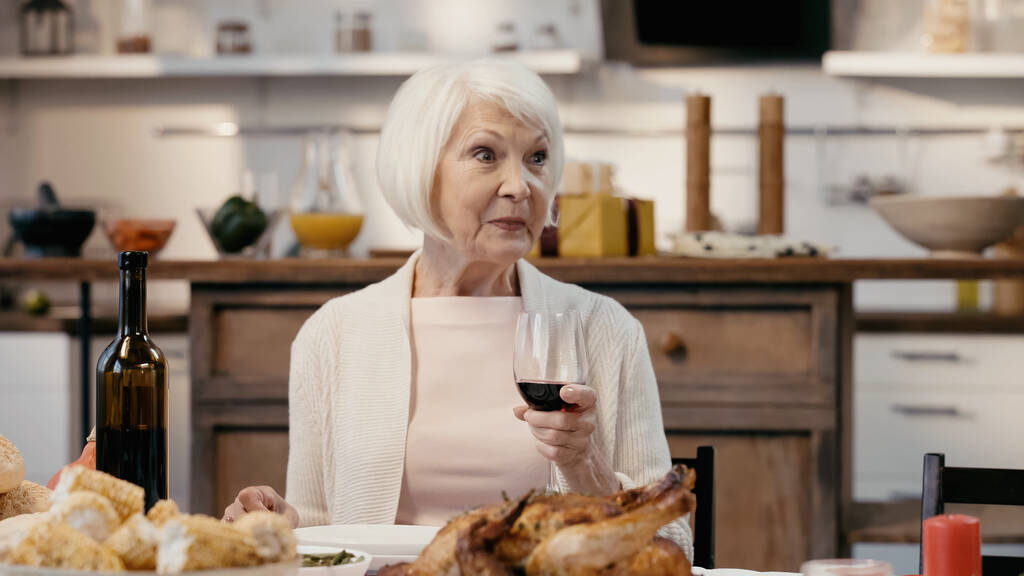 ευτυχισμένη ηλικιωμένη γυναίκα κρατώντας ένα ποτήρι κόκκινο κρασί κατά τη διάρκεια του δείπνου των Ευχαριστιών - Φωτογραφία, εικόνα