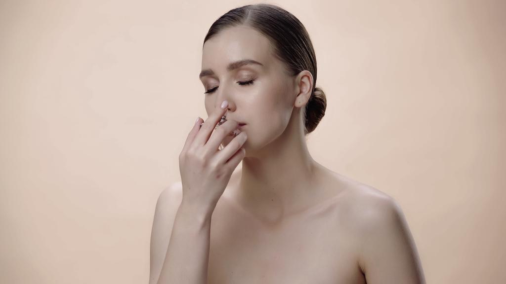 young woman with bare shoulders smelling luxurious perfume isolated on beige - Foto, afbeelding